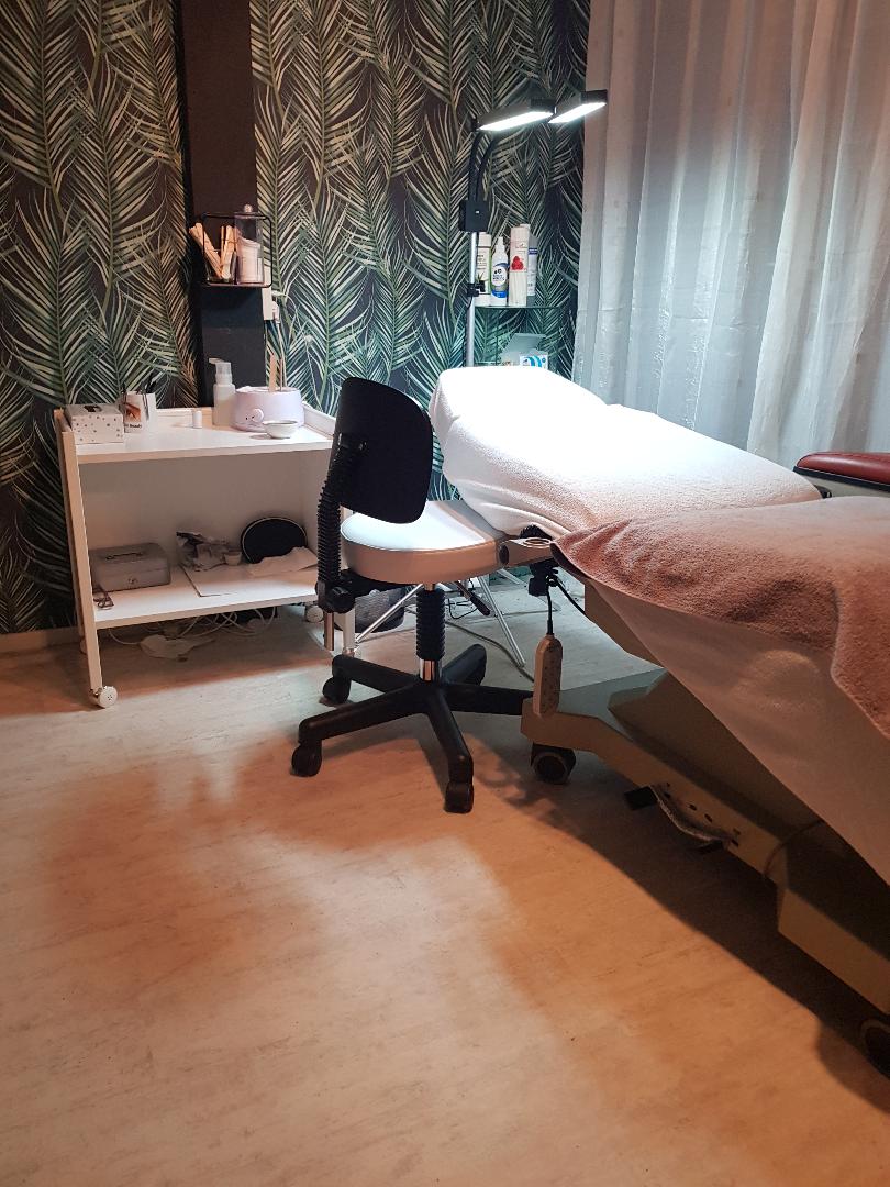 De behandelkamer van Noor Beauty met behandelbank, stoel en palmbladbehang